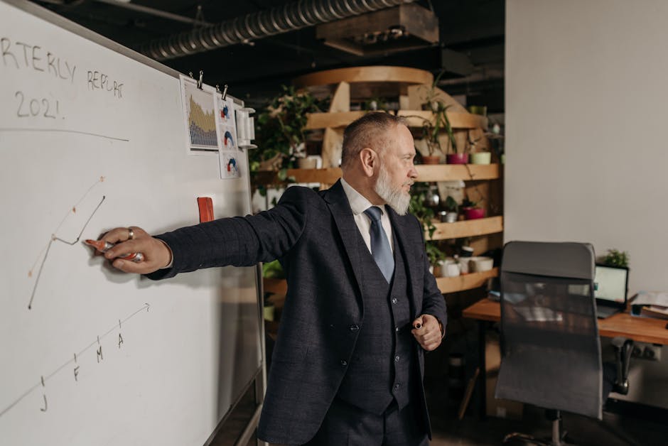 A businessman in a suit presents a quarterly report on a whiteboard in a modern office setting.